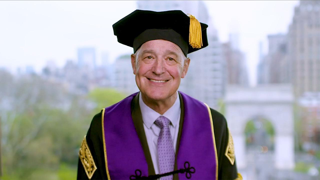 NYU president Andrew Hamilton wearing NYU regalia and giving a recorded speech from NYC. 